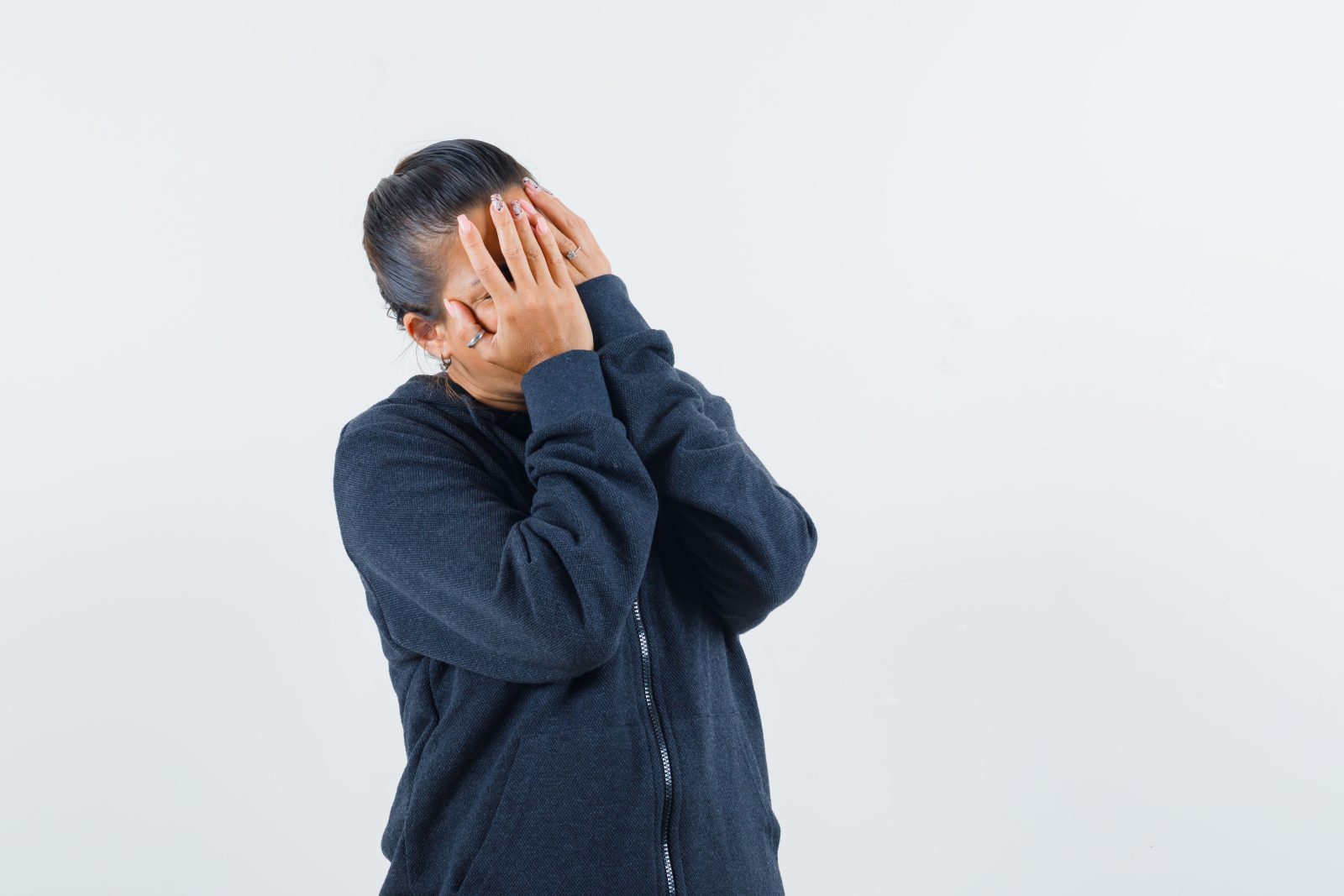 dark-haired-woman-covering-face-with-hands-jacket-looking-upset