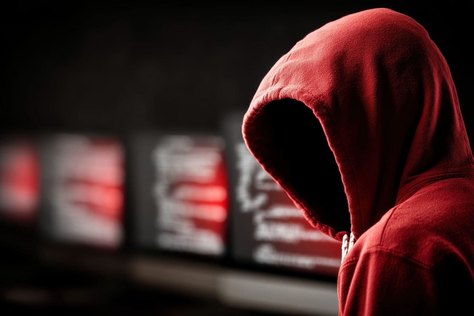 wide-view-anonymous-figure-red-hoodie-facing-multiple-computer-screens-with-code-display 1